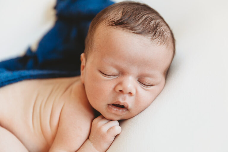 Profile shot of sleeping baby posed on side with soft navy wrap on a smooth white studio backdrop at Reflection Images by Tracy Rowell in Florence SC