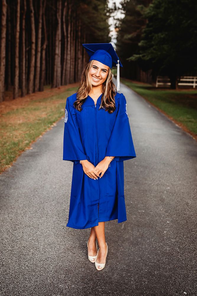 Senior session photo taken in rustic bridge at golden hour, showing a laughing pose blue cap and gown graduate