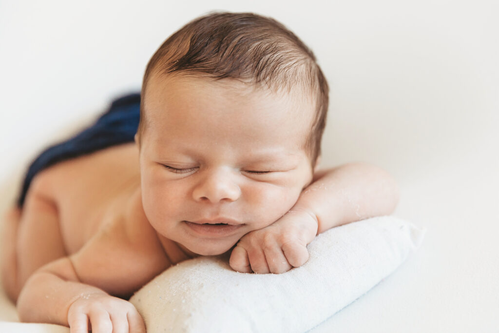 Baby lying on tiny white pillow with gentle smile and dark blue wrap at Reflection Images by Tracy Rowell in Florence SC