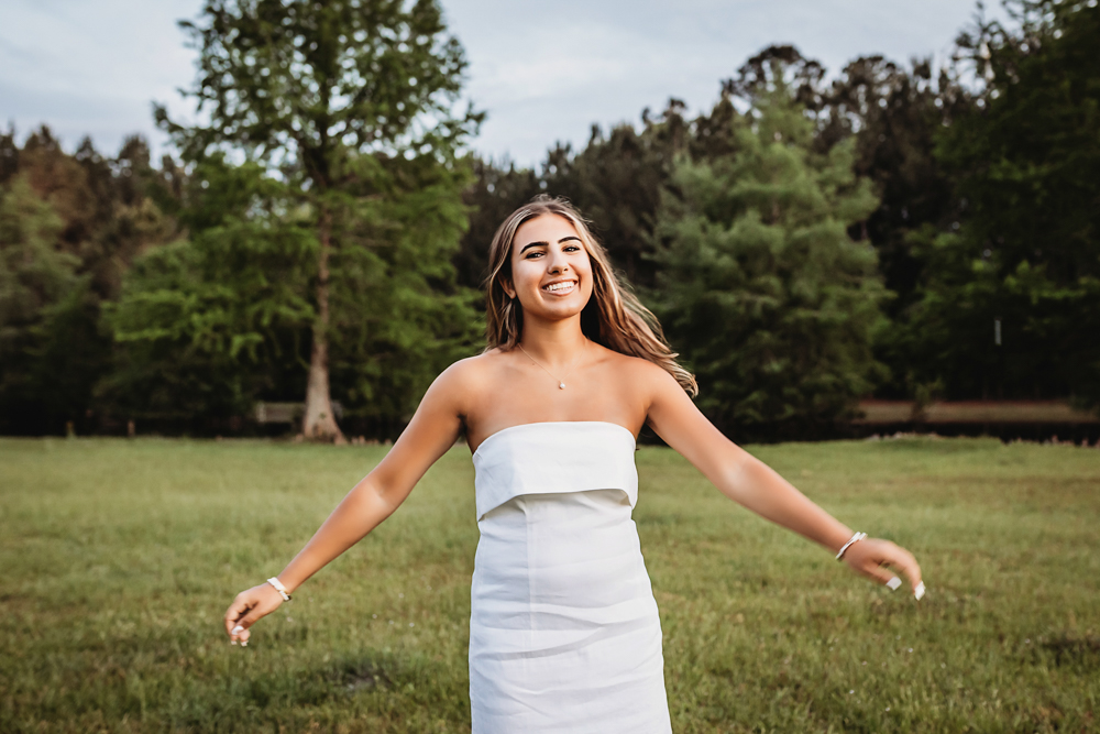 Senior session photo taken in open field at golden hour, showing a twirling pose in casual style from a eye-level angle