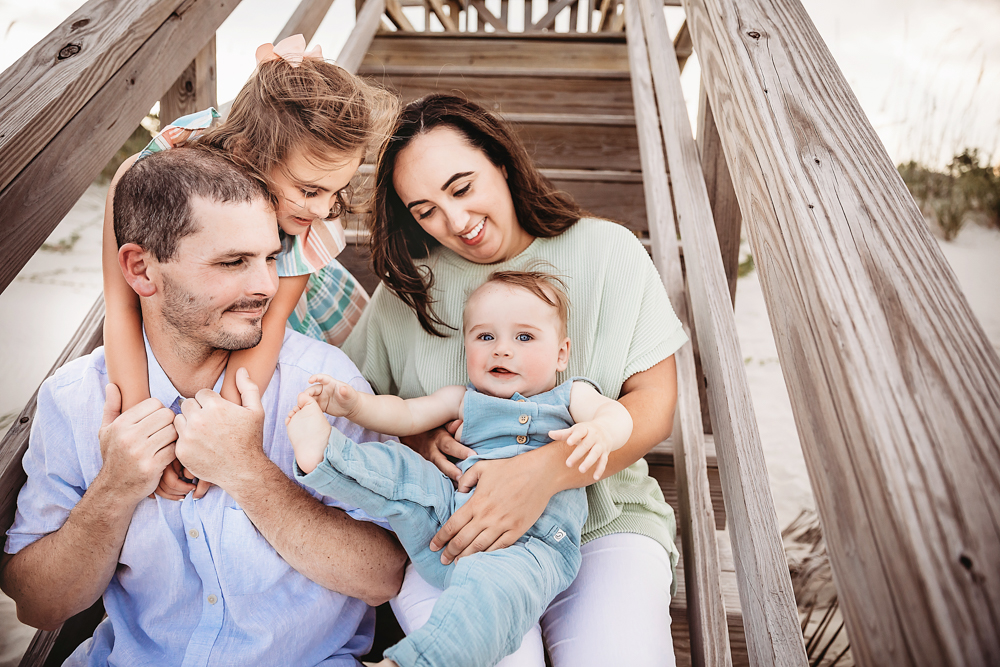The Skinner family laughing and snuggling close on beach stairs in a candid layered group pose at Reflection Images by Tracy Rowell in Florence SC