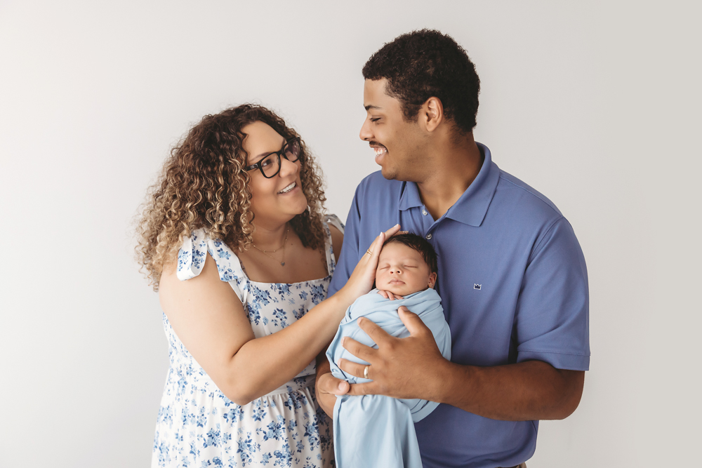 Mom and dad smiling at each other while holding baby Liston wrapped in soft blue at Reflection Images by Tracy Rowell in Florence SC