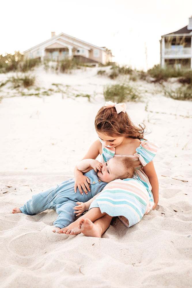 Stella holding Cole close while seated in the sand, her bow visible and both barefoot at Reflection Images by Tracy Rowell in Florence SC
