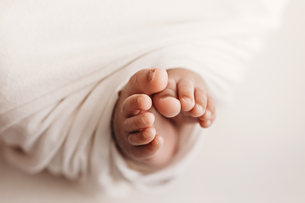 Close-up of Braylens delicate toes peeking from soft white swaddle with creamy studio light at Reflection Images by Tracy Rowell in Florence SC