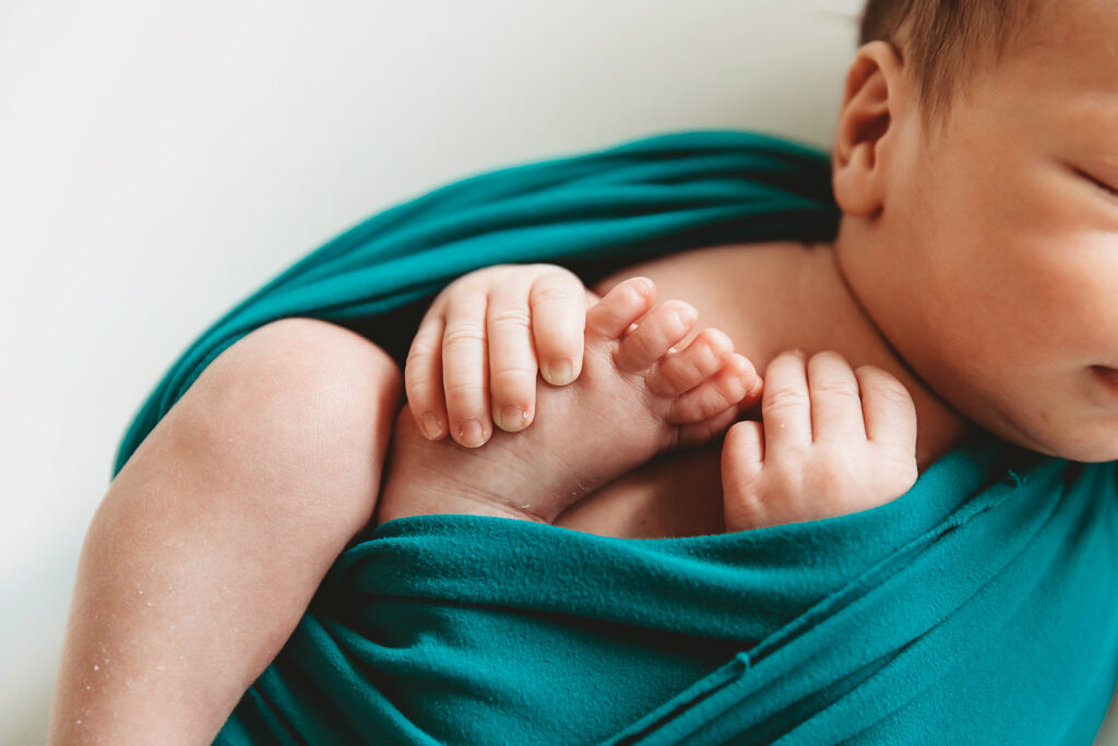 Close-up of a newborn baby's hands holding its feet, wrapped in green cloth