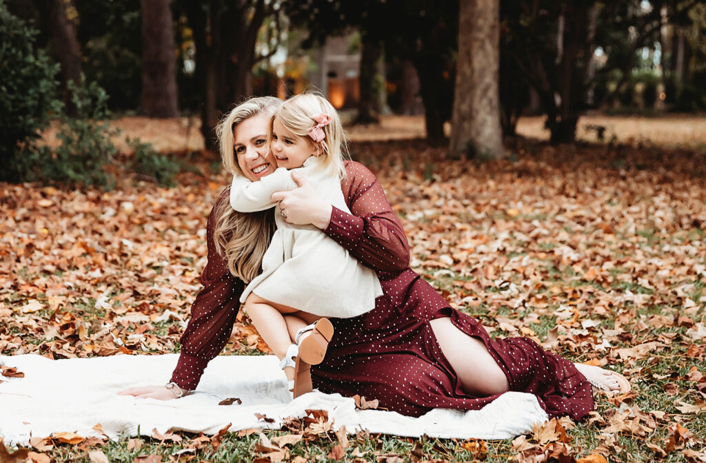 Mom and toddler girl hugging on white blanket in the park
