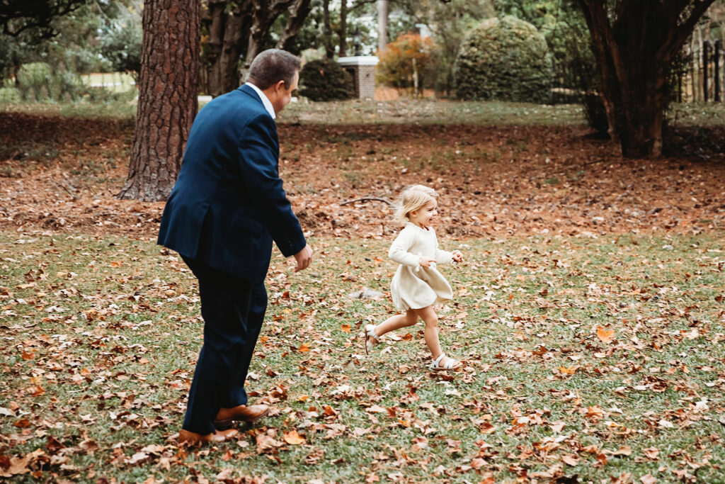 Dad and daughter running playfully through autumn leaves