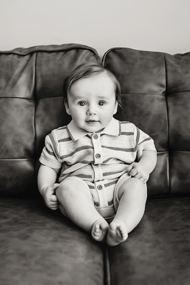 Black and white baby sitting on couch in striped romper, newborn photographer near Florence SC