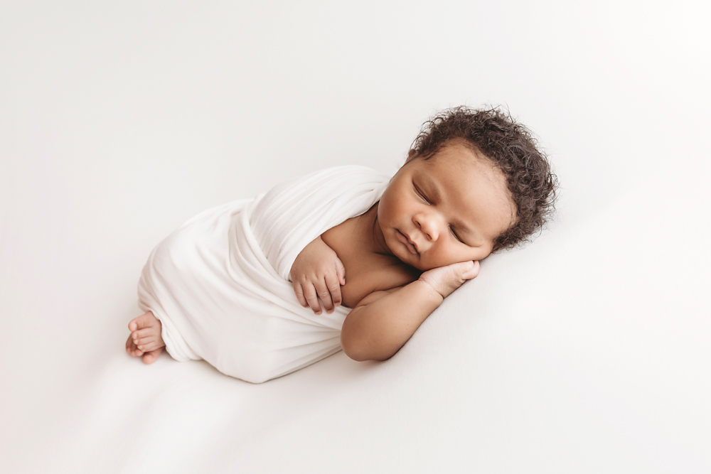 Braylen peacefully napping on his side, wrapped in white, with curls visible on clean white studio setup at Reflection Images by Tracy Rowell in Florence SC