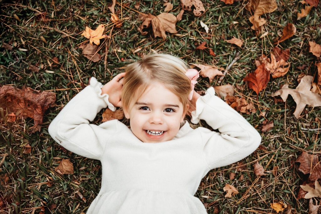Happy little girl lying on grass smiling with bow in hair