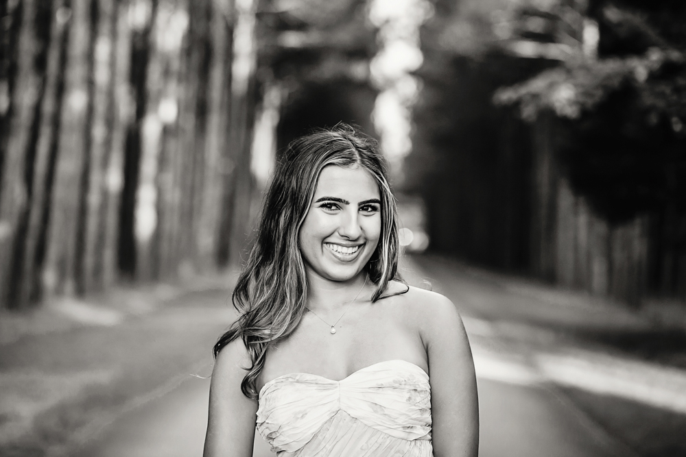Black and white Senior session photo taken in rustic bridge at golden hour, showing a looking-away pose in casual style from a eye-level angle