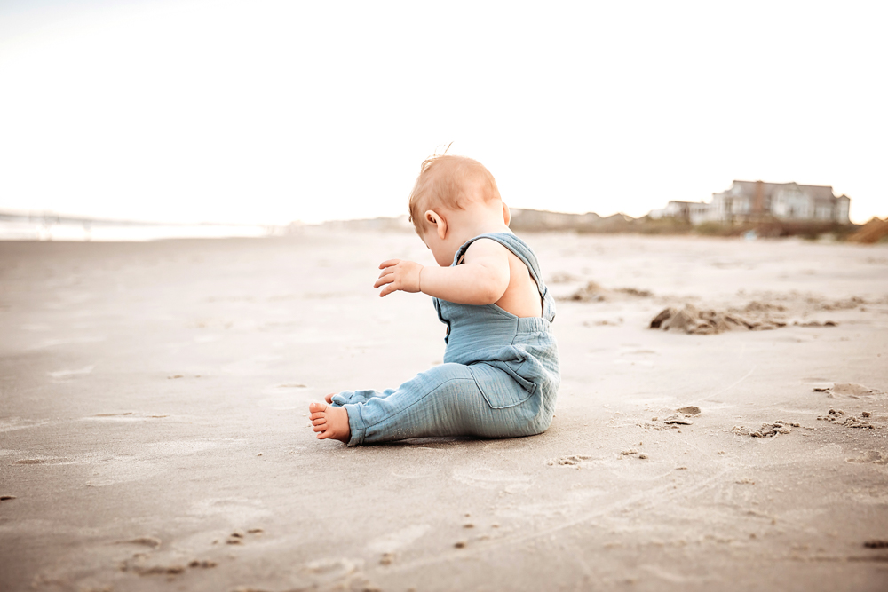 Cole seated solo in the sand facing down with soft evening light and beach cottages in distance at Reflection Images by Tracy Rowell in Florence SC
