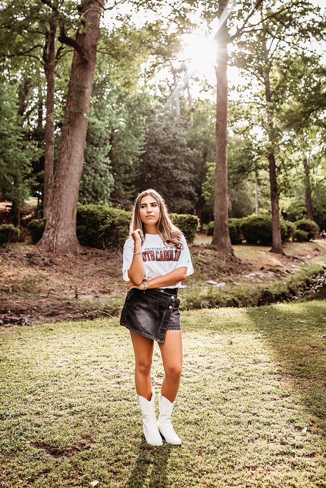 Senior session photo taken in open field at golden hour, showing a laughing pose in USC shirt and denim skirt from a close-up angle