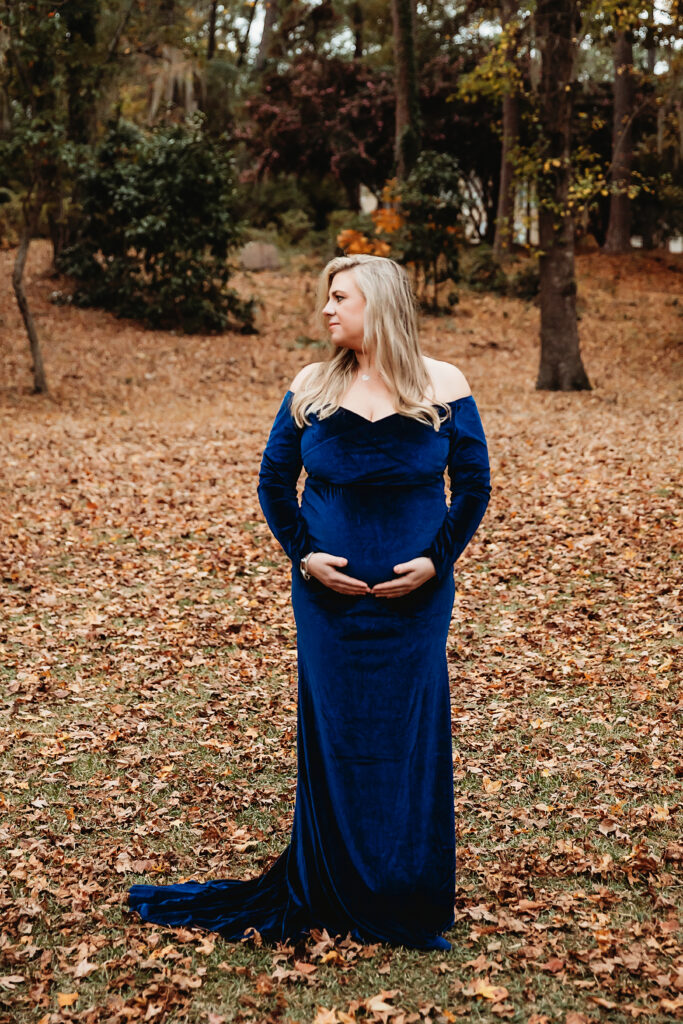 Expecting mother in blue velvet gown cradling belly in fall forest