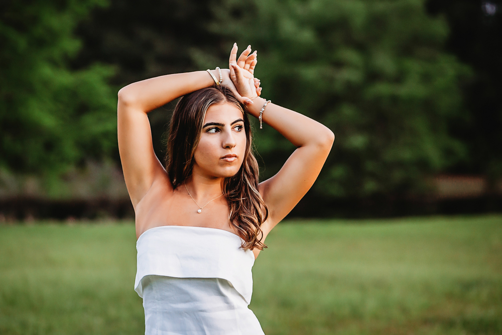 Senior session photo taken in golden hour at golden hour, showing a twirling pose in white dress from a full-body angle