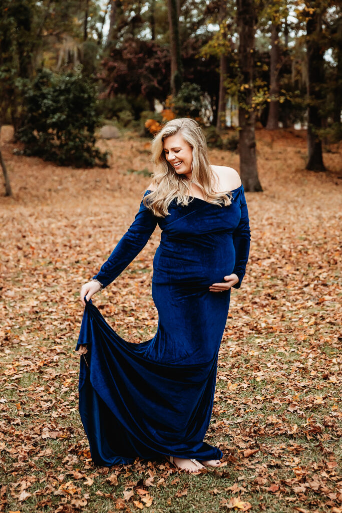 Joyful mother-to-be barefoot in blue dress smiling in leaves