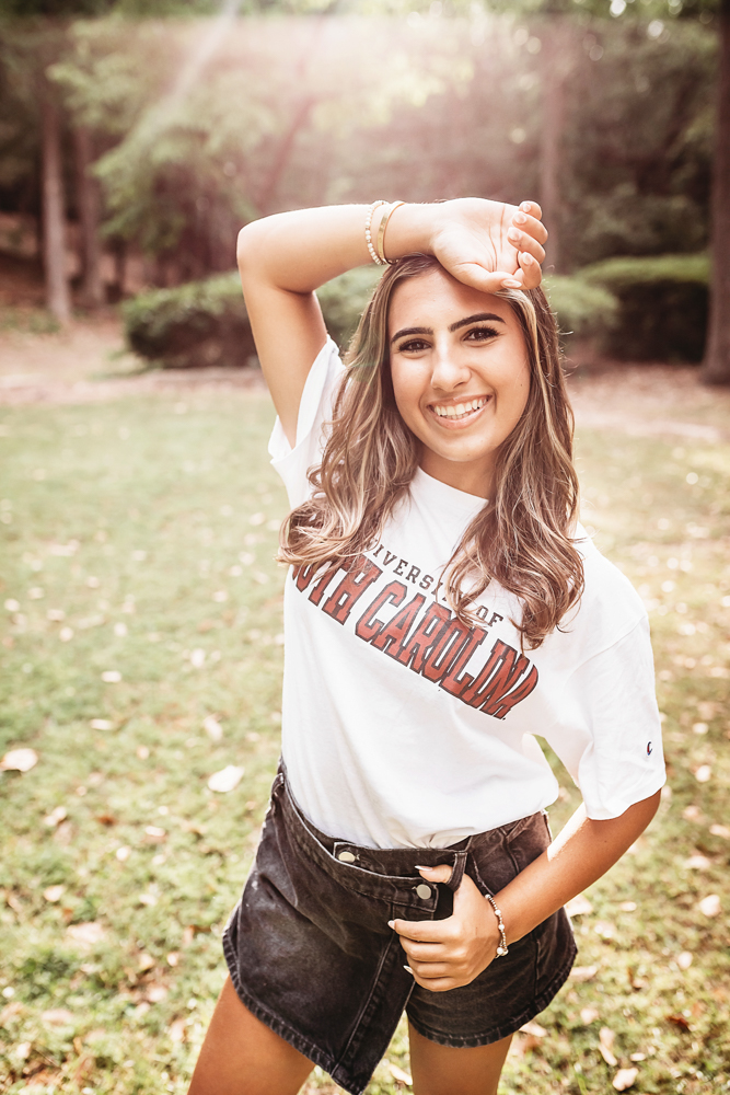 Senior session photo taken in sunlit trail at golden hour, showing a standing pose in Gamecock shirt from a profile angle