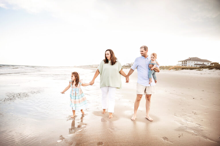 Skinner family walking hand in hand at the shoreline with reflections in wet sand and pastel skies at Reflection Images by Tracy Rowell in Florence SC