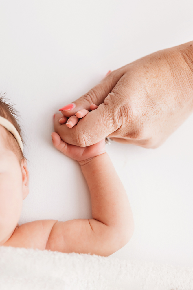 Close-up of a newborns hand gently holding mothers hand with pink-painted nails.