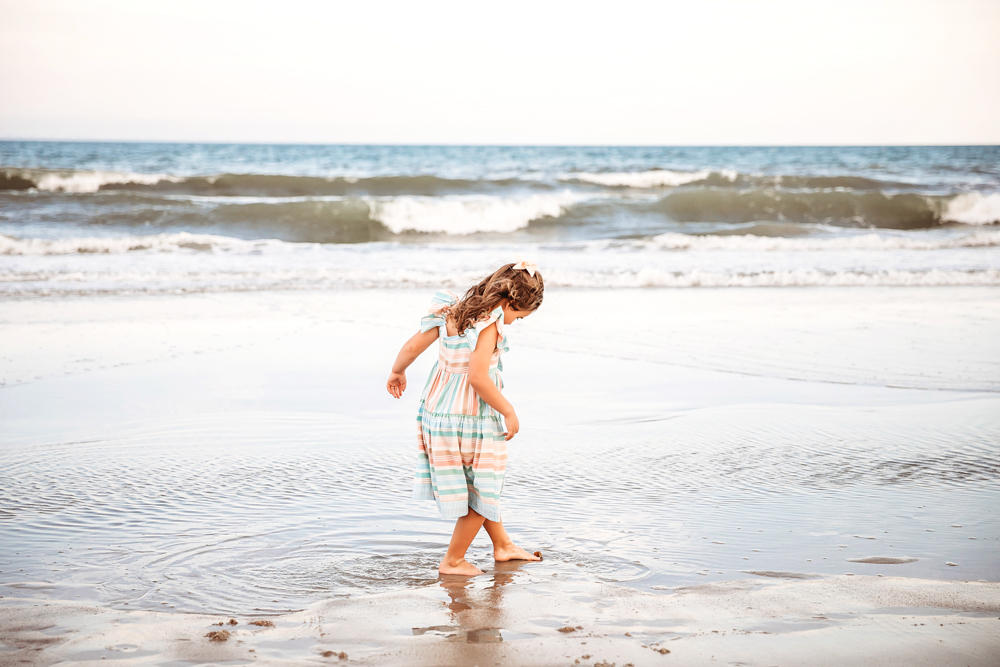 Little girl tiptoes in a shallow tide pool near the edge of the shore, curious and playful.