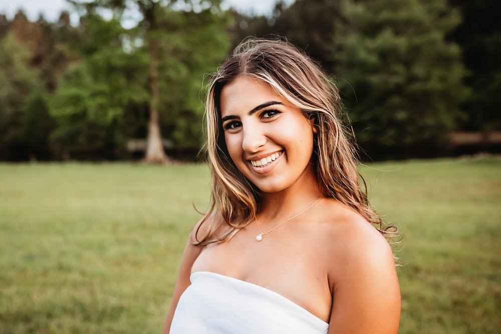 Senior session photo taken in golden hour at golden hour, showing a laughing pose in white boots from a over-the-shoulder angle