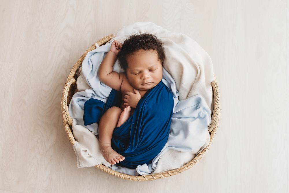 Braylen swaddled in deep blue wrap, sleeping serenely on white background