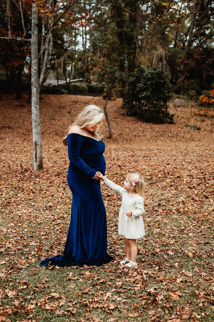 Sweet moment of mom and daughter holding hands and smiling in wooded area with orange fall leaves in Florence SC