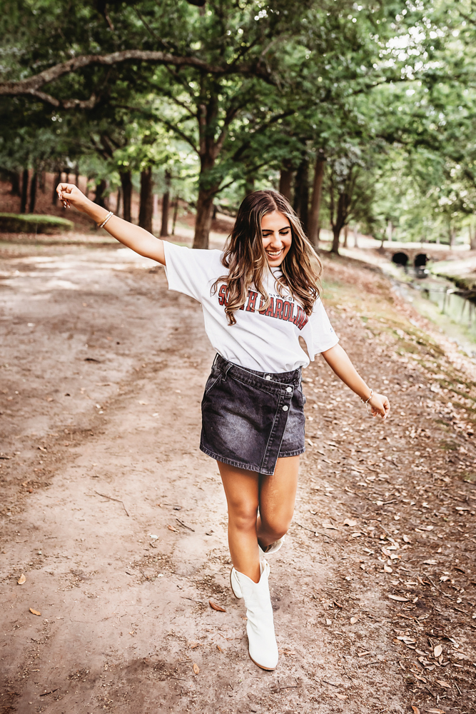 Senior session photo taken in wooded park at golden hour, showing a twirling pose in Gamecock flag from a profile angle