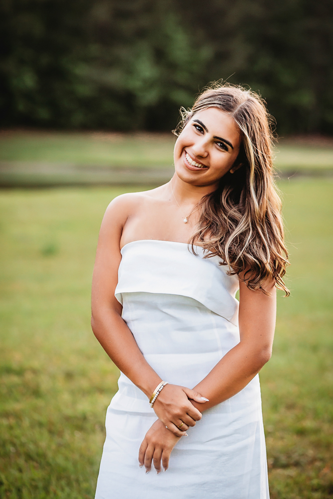 open field at golden hour, showing a smiling pose in USC shirt and denim skirt from a close-up angle at Reflection Images by Tracy Rowell in Florence SC.