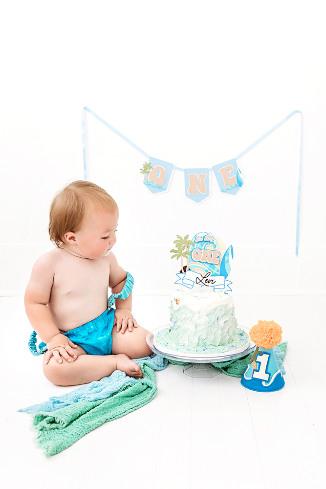 Levi sitting in front of a blue ocean-themed cake with matching banner and decorations for his cake smash session at Reflection Images by Tracy Rowell in Florence SC