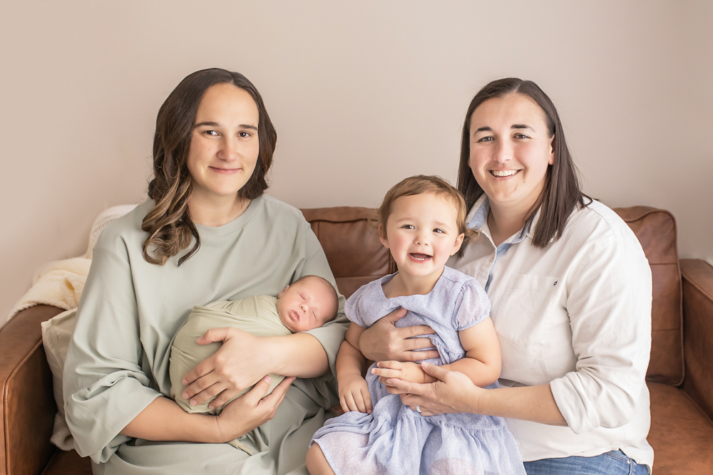 two moms with toddler and newborn family portrait on caramel couch Florence SC