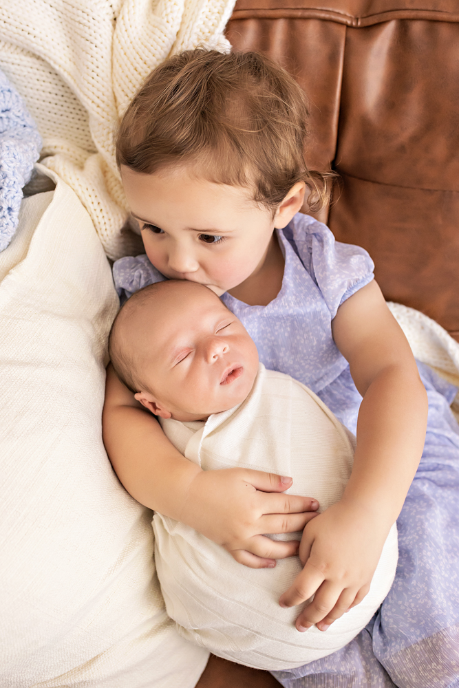 toddler kissing newborn brothers forehead while holding him on couch Florence SC