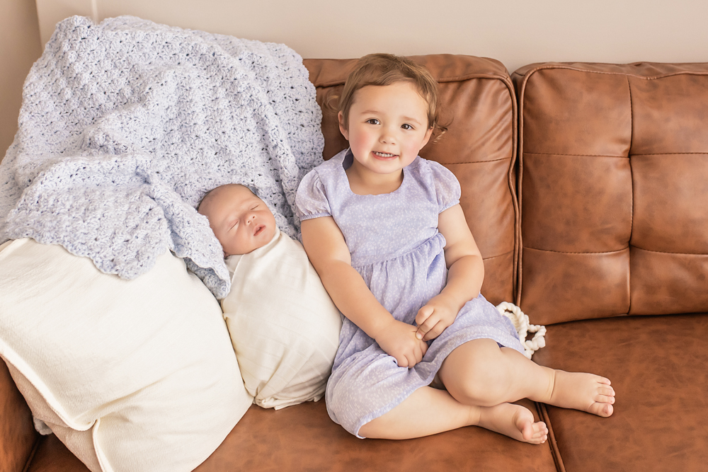siblings seated on leather sofa baby swaddled with blue knit blanket Florence SC