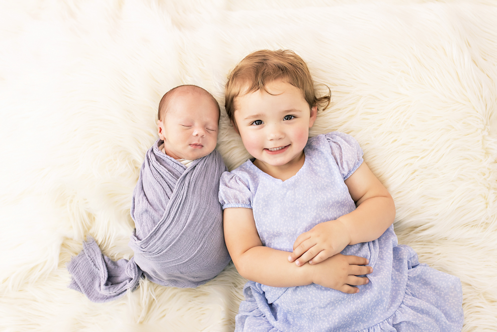 siblings on white flokati newborn in lavender wrap sister in lilac dress Florence SC studio