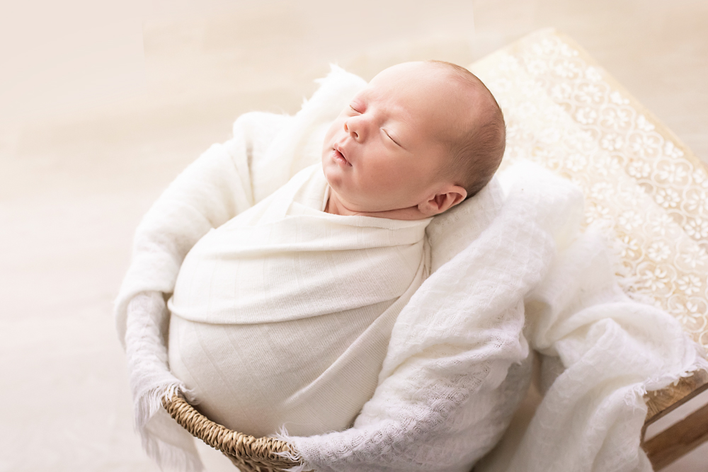 side view newborn in ivory wrap reclining in basket newborn props on patterned bench Florence SC