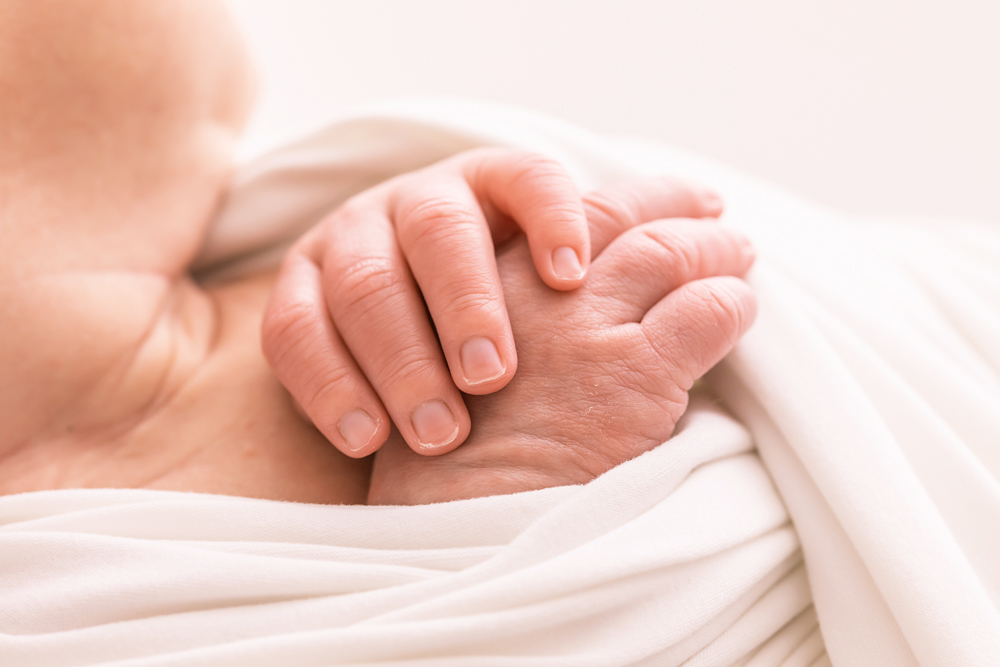close-up of newborn folded hands resting on chest in white wrap Florence SC