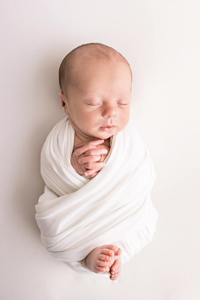 newborn in pure white wrap with folded hands and exposed toes on white Florence SC