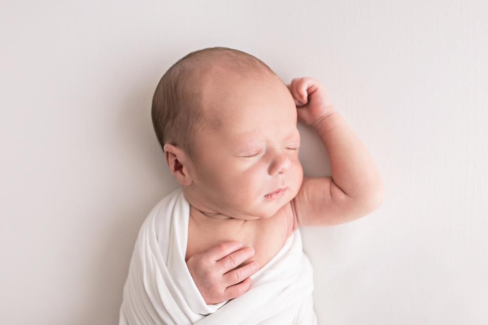 side profile newborn Walker in white swaddle one arm up on white beanbag Florence SC