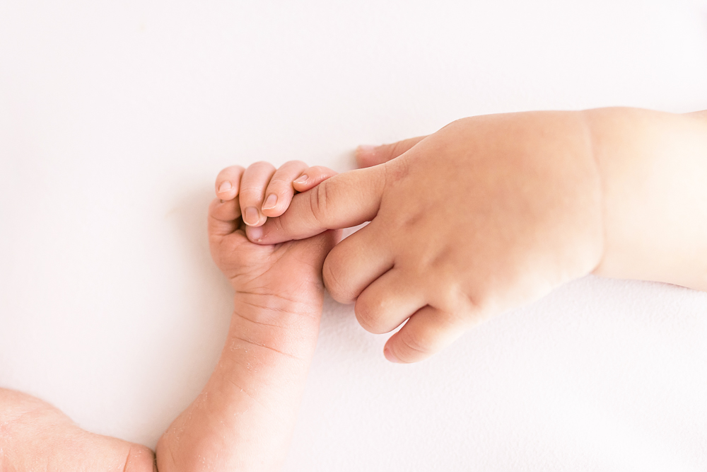 toddler sister holding newborn brothers finger on white blanket Florence SC