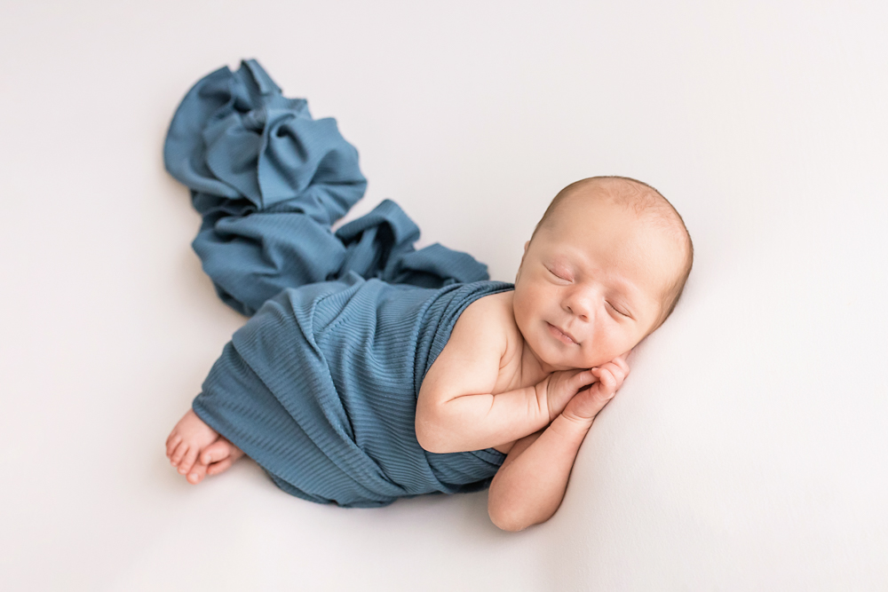 side-lying newborn in teal ribbed wrap with trailing fabric on white Florence SC