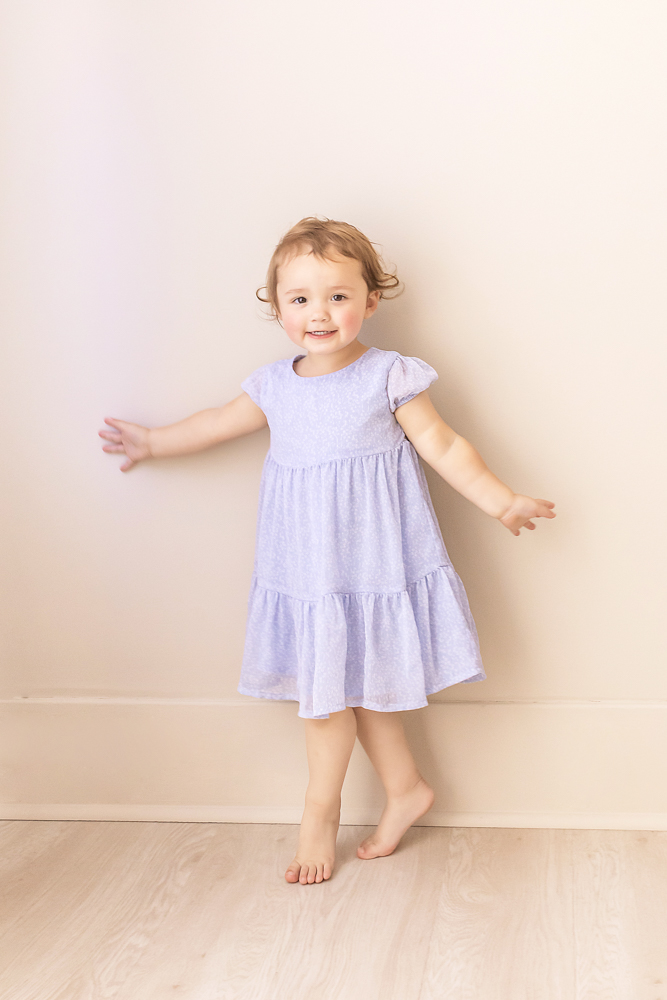 toddler sister twirling in light purple dress against neutral wall Florence SC
