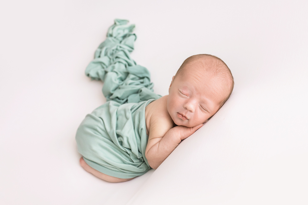 newborn in soft mint wrap side-lying with long fabric tail on white Florence SC