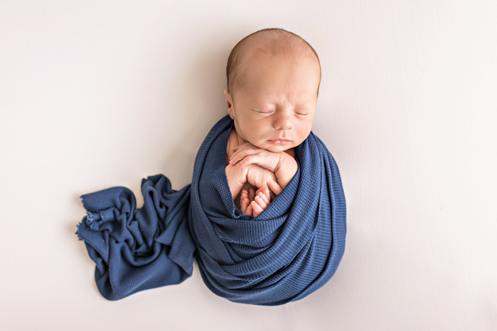 newborn Walker swaddled in navy waffle wrap hands tucked under chin on white beanbag Florence SC
