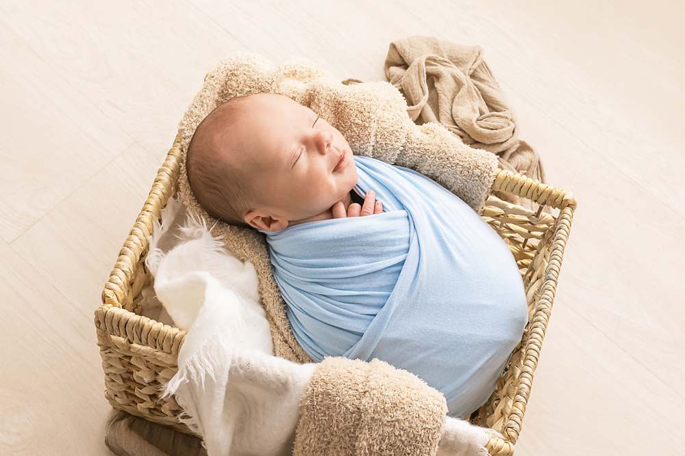 newborn in light blue wrap sleeping in woven basket with cream throws Florence SC
