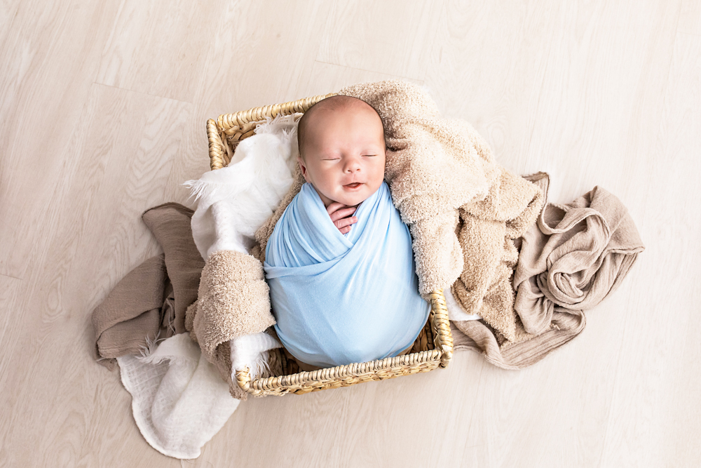 overhead of newborn swaddled in pale blue wrap smiling in basket with tan blankets Florence SC