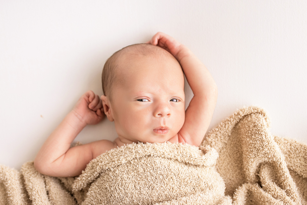 awake newborn Walker under tan terry blanket arms stretched on white bed Florence SC