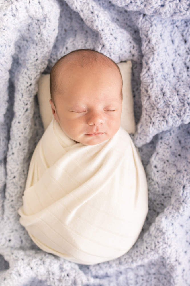 professional images of newborn swaddled in white on soft blue crochet blanket overhead Florence SC Reflection images
