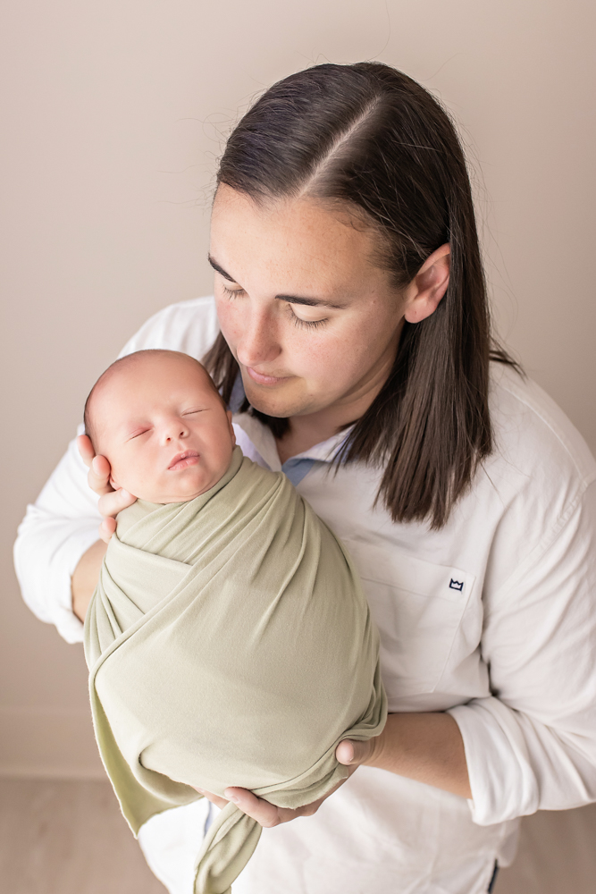 mom holding newborn in sage green wrap looking down neutral studio Florence SC