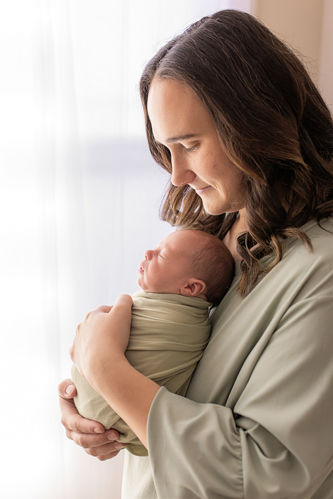 mother cuddling newborn by bright window baby swaddled in sage wrap natural light Florence SC photography