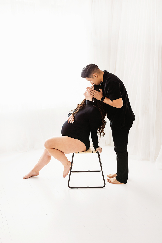 Buenrostro couple kiss maternity in bright natural light and clean studio backdrop at Reflection Images by Tracy Rowell in Florence SC